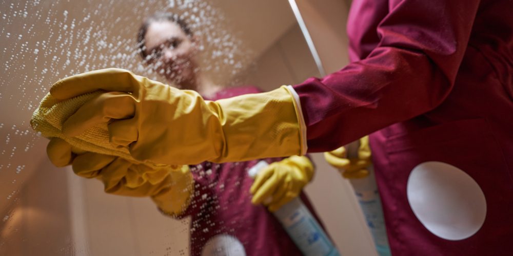 Dark-haired professional female cleaner removing drops of cleaning solution from mirrored surface